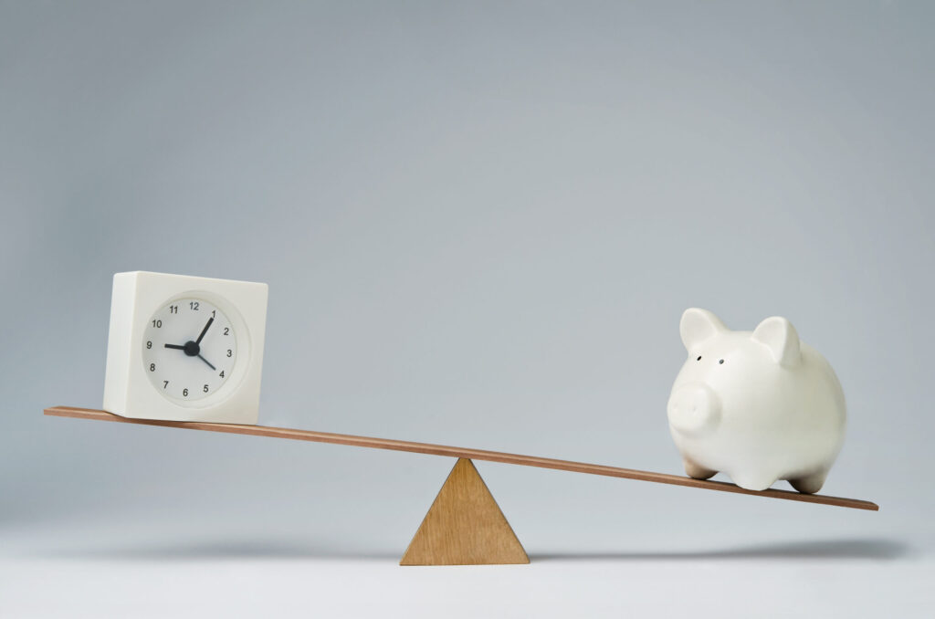 A visual metaphor of striking the Balance Between Immediate Results and Long-Term Success with a clock on the slightly higher left side of a seesaw with a piggy bank on the lower opposite end